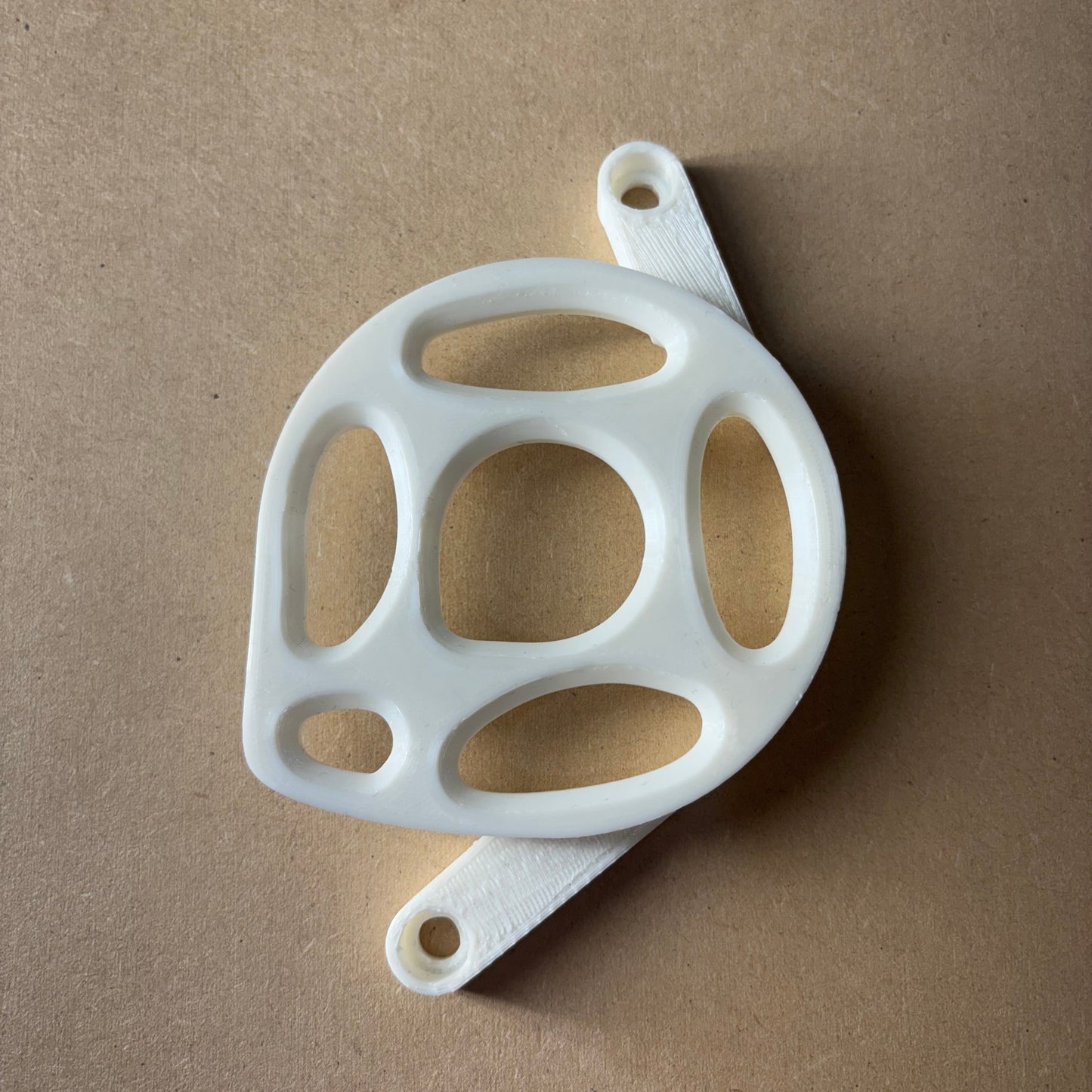 White plastic component with multiple holes on a brown background